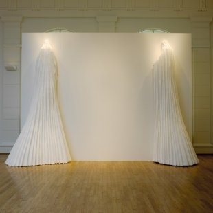 A sculpture composed of a large white wall and two large white dresses