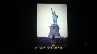 A film still of a person of Asian descent standing in front of the Statue of Liberty