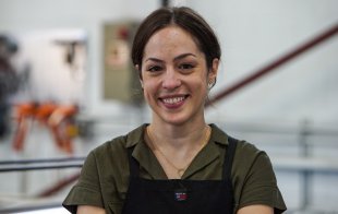 A woman with brown hair pulled back in a ponytail wearing a green shirt and black apron