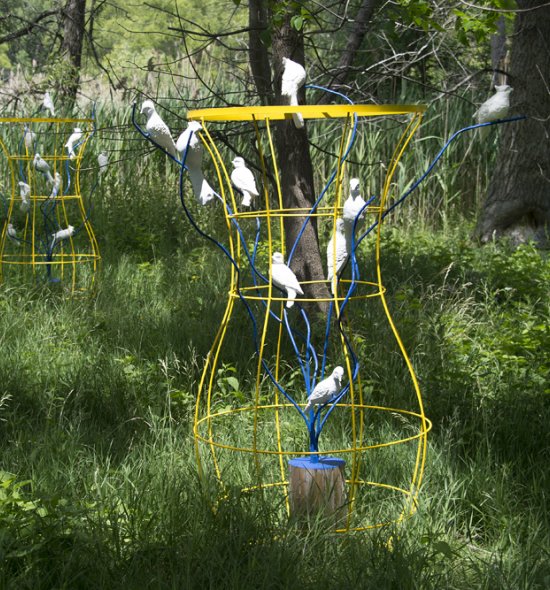 Two yellow wire sculptures with white birds sit in a green field
