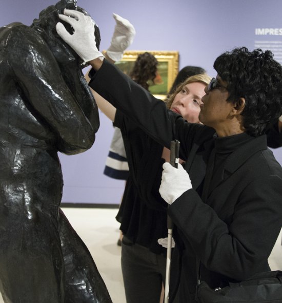 A woman with visual impairments touches a sculpture with gloves on