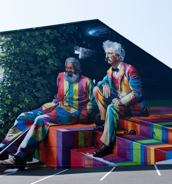 A large colorful mural of an African American man and a white man sitting next to each other on steps