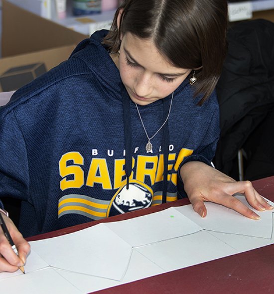 A girl in a Buffalo Sabres sweatshirt drawing in a classroom