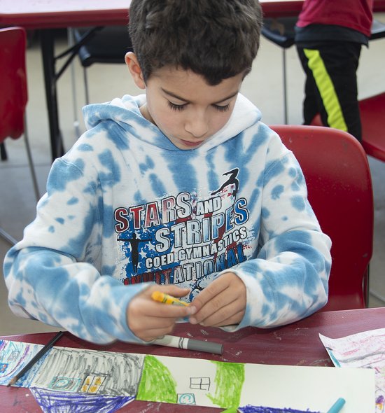 A boy with a blue and white sweatshirt makes art in a classroom