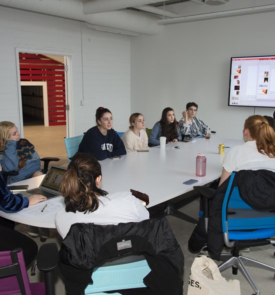 A group of teens sitting around a table looking at a large screen on the wall