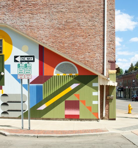 A colorful mural with geometric shapes and colored backgrounds on the side of a building on a street corner