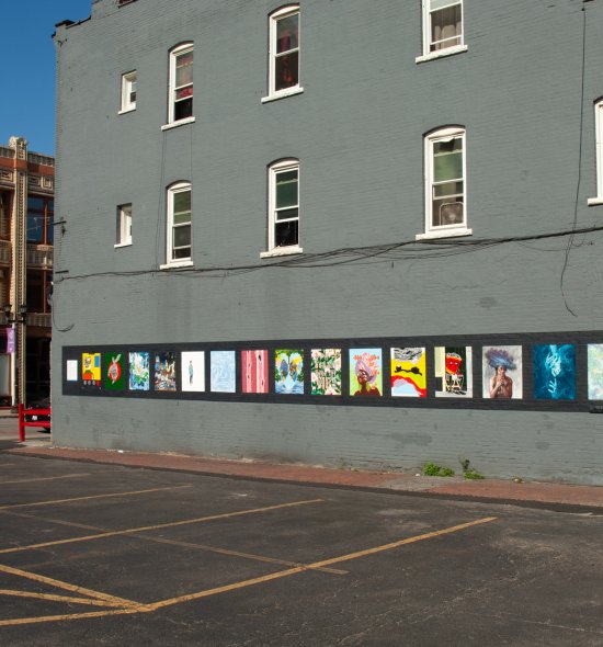 An exterior wall of a three-story building with 16 paintings side by side at the first floor level