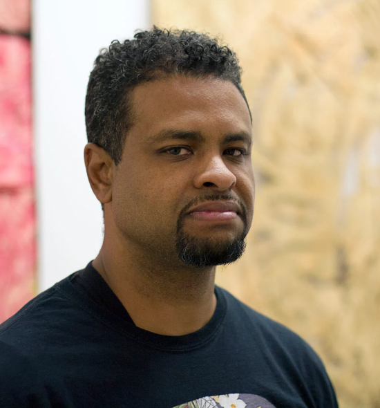 Man of medium-dark skin tone with goatee in black shirt, seen from the shoulders up