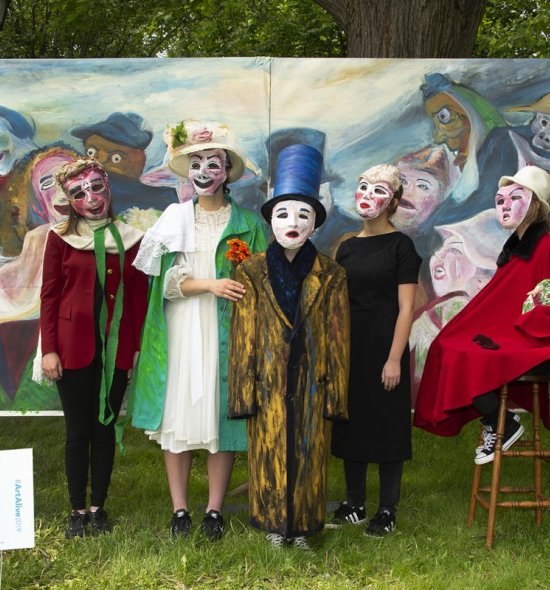 A group of high school students dressed up as figures in a painting that is behind them 