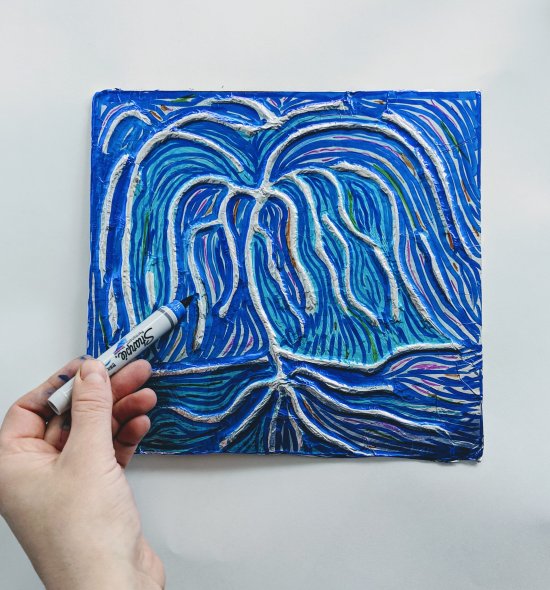 A person coloring with blue marker around a silver tree
