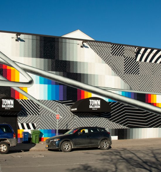 A large mural on the side of a building with sections of bold color and sections of black and white stripes