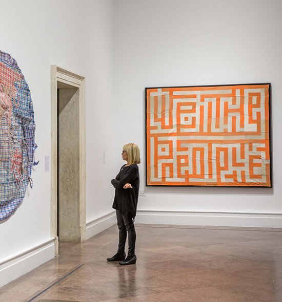 A woman dressed in all black looking at a large colorful work hanging on the wall in front of her