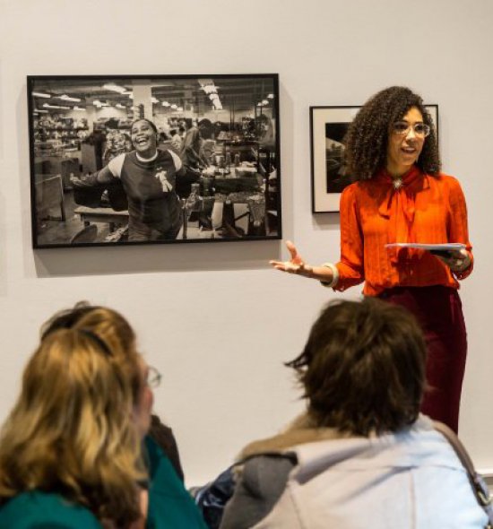 Artist Julia Bottoms in front of a black-and-white photograph that she is discussing with a group of people