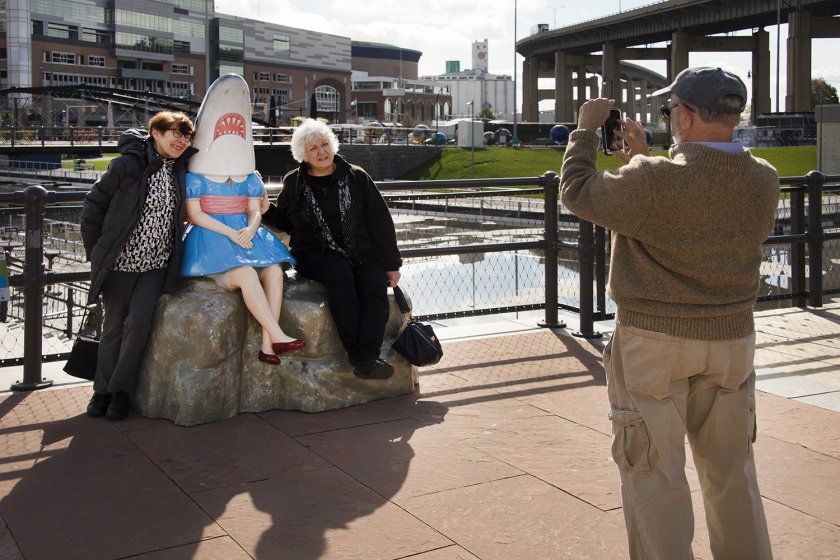 Two women taking a photo with Casey Riordan&#039;s Shark Girl​​​​​​​, 2013, at Canalside Buffalo