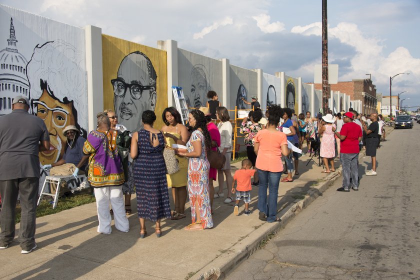 People gathered for a community event at The Freedom Wall on August 15, 2017. In back, artist John Baker at work on a portrait of Shirley Chisholm, artist Julia Bottoms at work on a portrait of Martin Luther King, Jr., and artist C